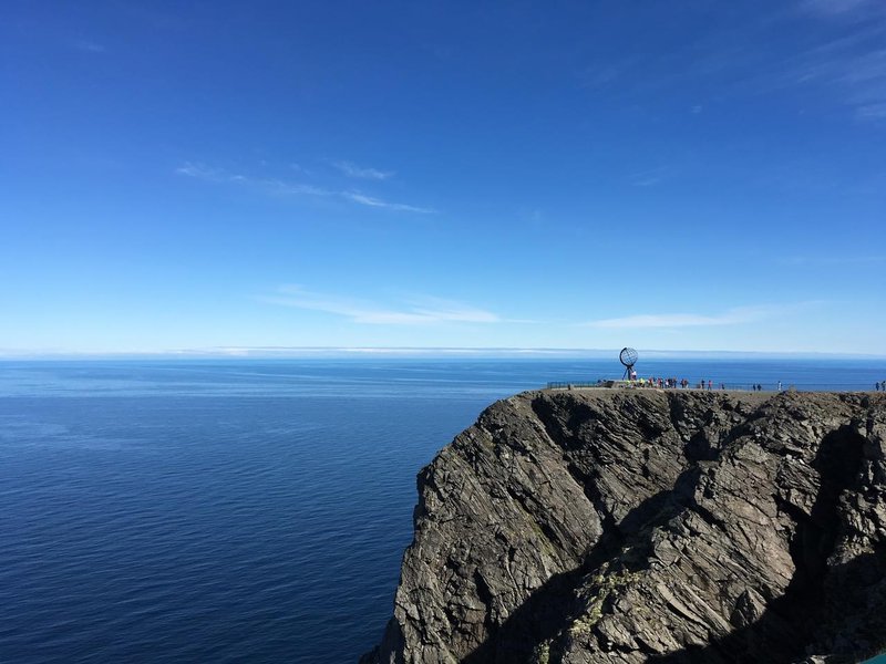 Blue sky and sea in the background with a cliff face to the rigt half, people atop the cliff.jpg